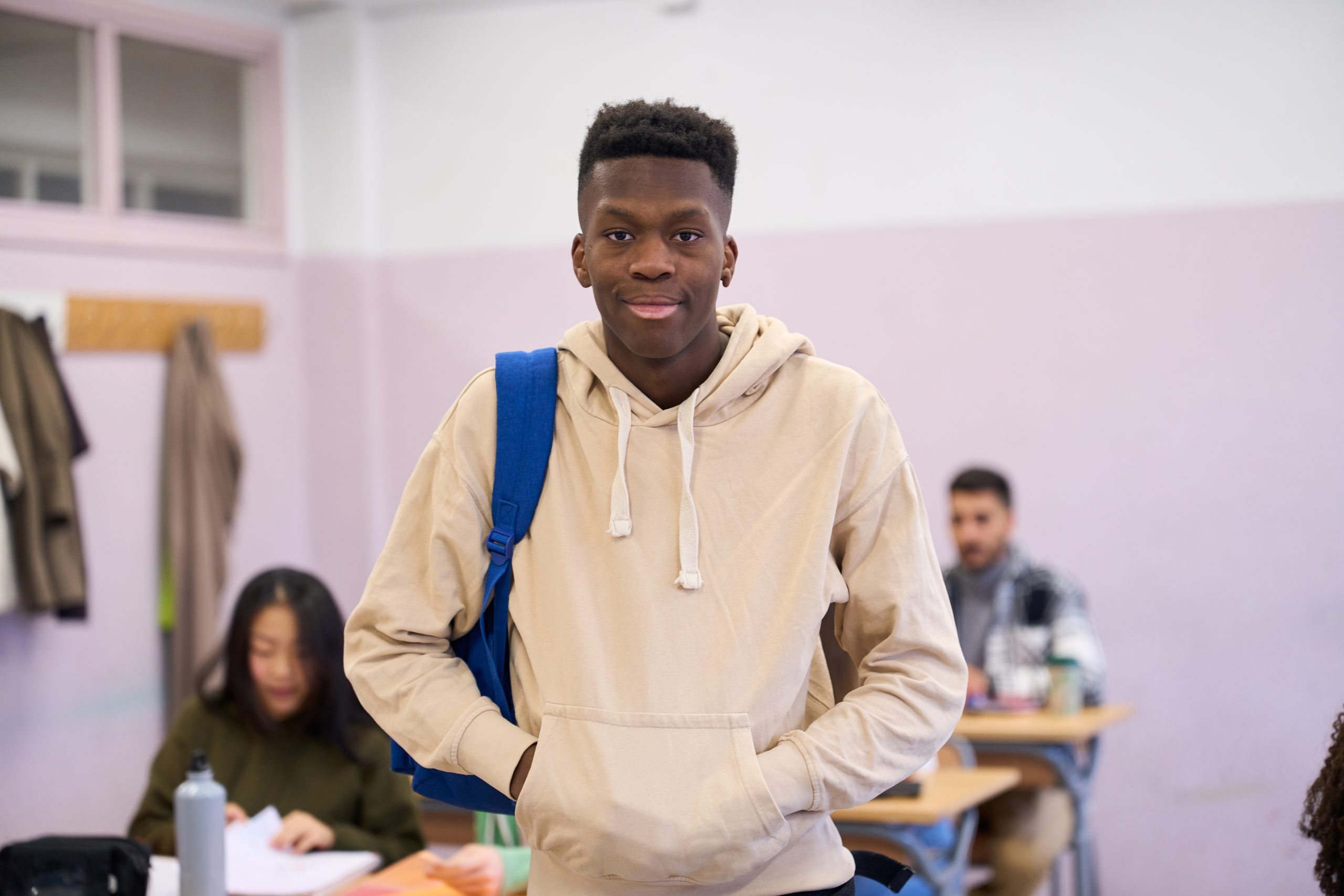Portrait of a confident african american male student standing in a classroom at the university institute with classmates in the background