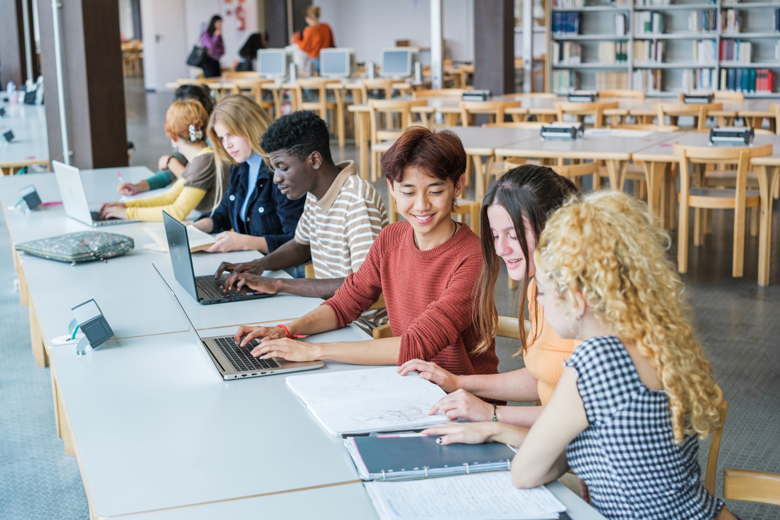 Group of students of different ethnicities studying in the university library - focus on Asian boy