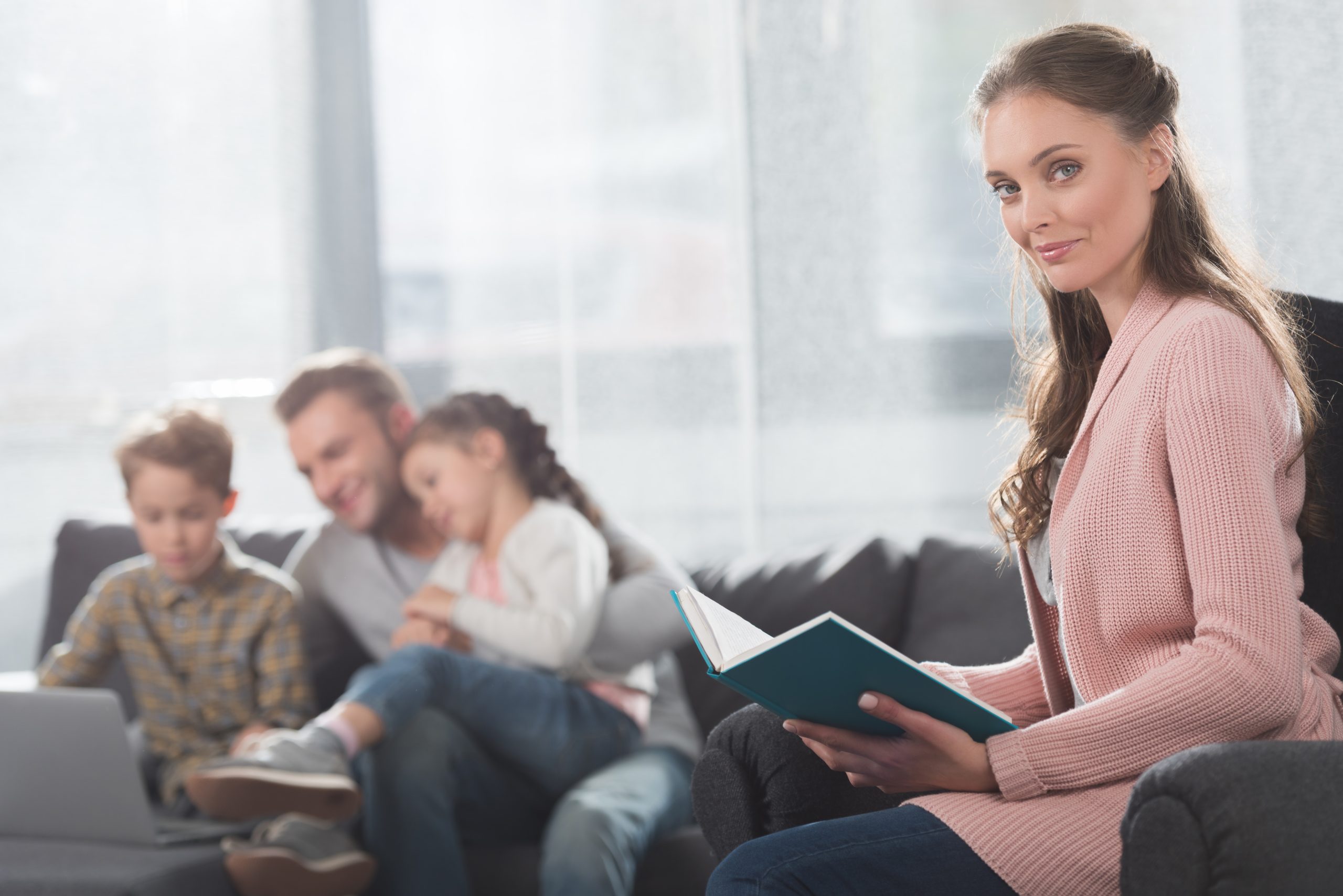 Mother reading book while father looking at the laptop with children