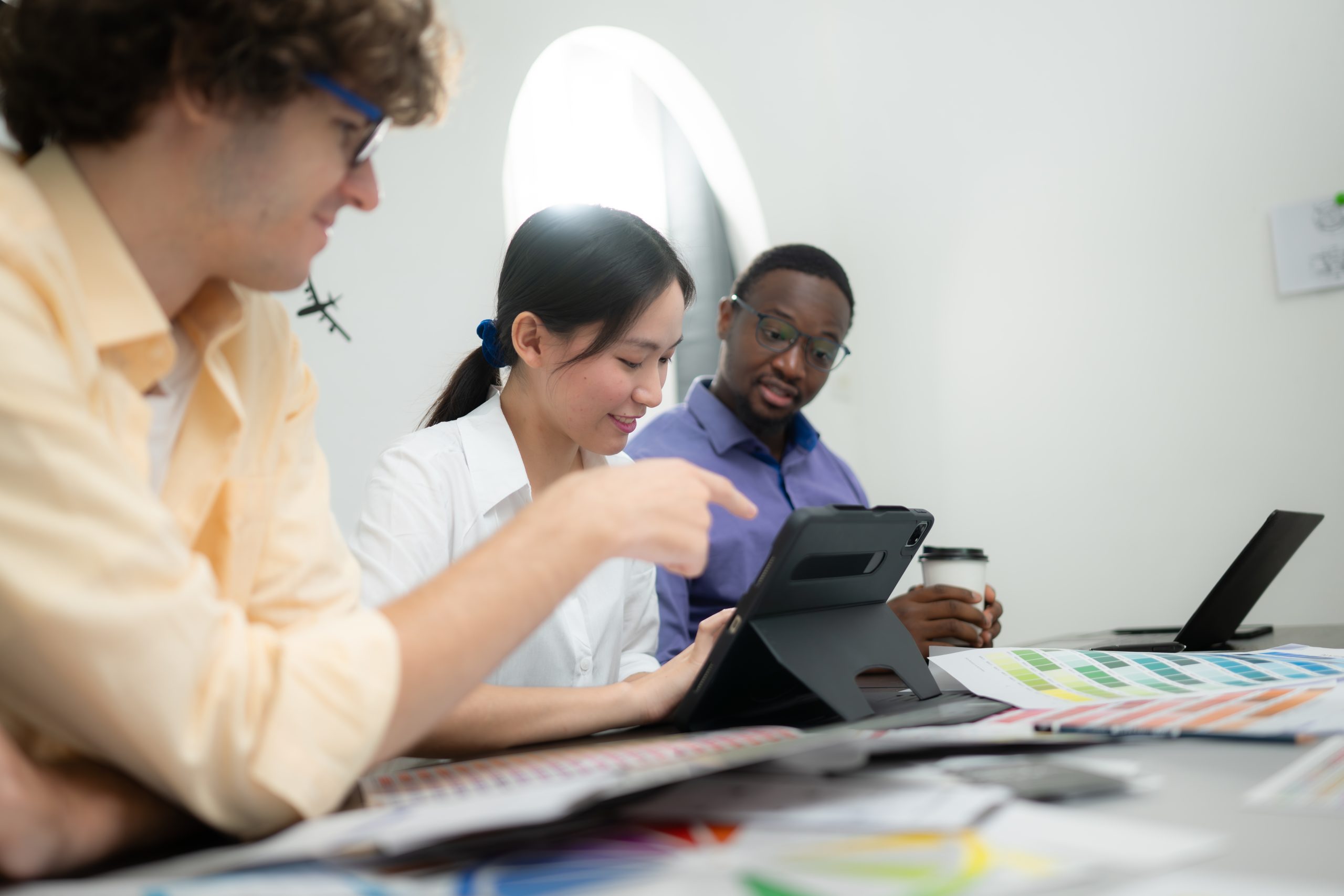 Multiethnic team of architects and designers are meeting to brainstorm design an application smartphone on a bright modern office working on a laptop.